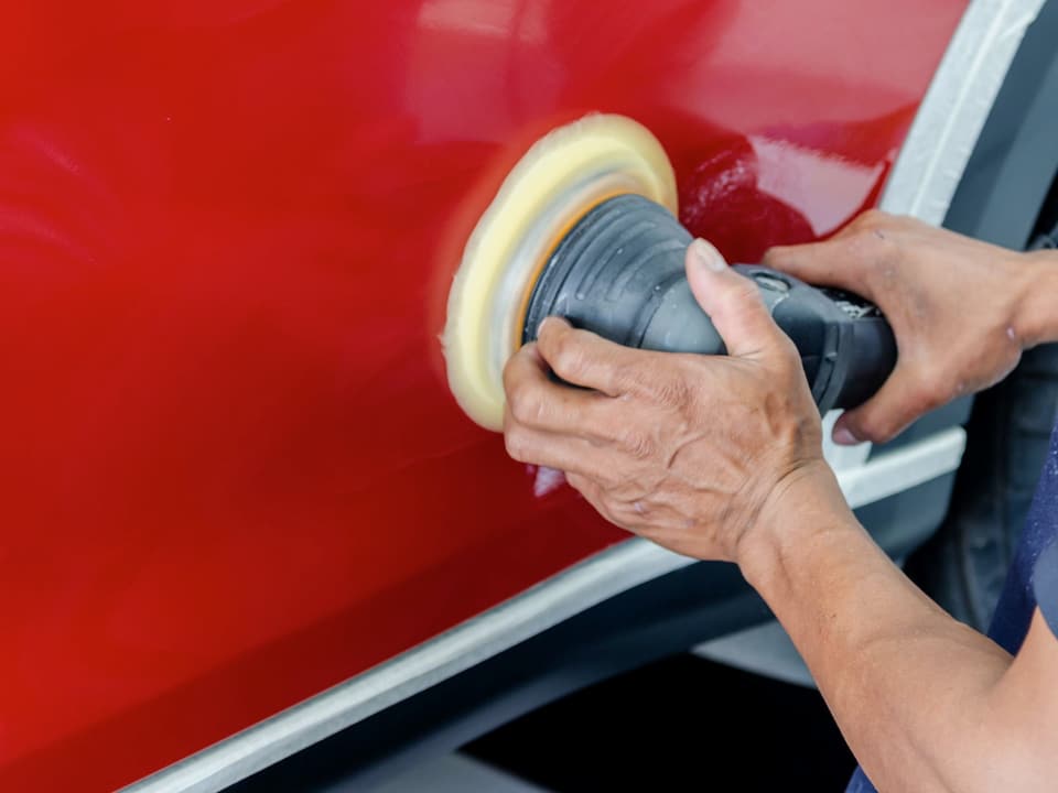 Hands using a polishing machine on a red car door